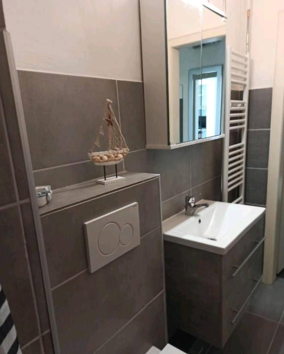 Badezimmer mit Waschbecken, Spiegel und Toilette. Dekoration mit Segelschiff.