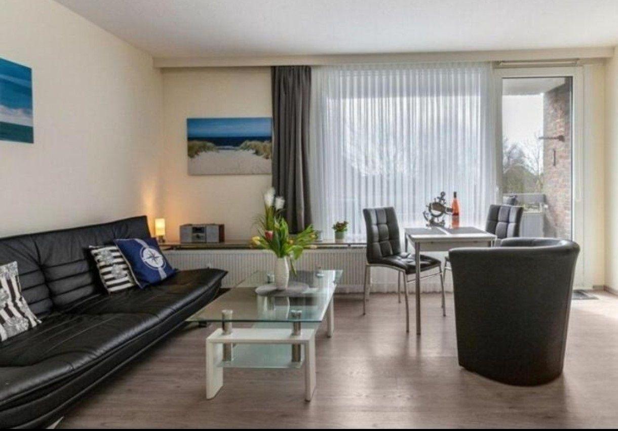 Wohn- und Essbereich mit Sofa, Tisch und Stühlen. Fenster mit Vorhängen und Wandbild.