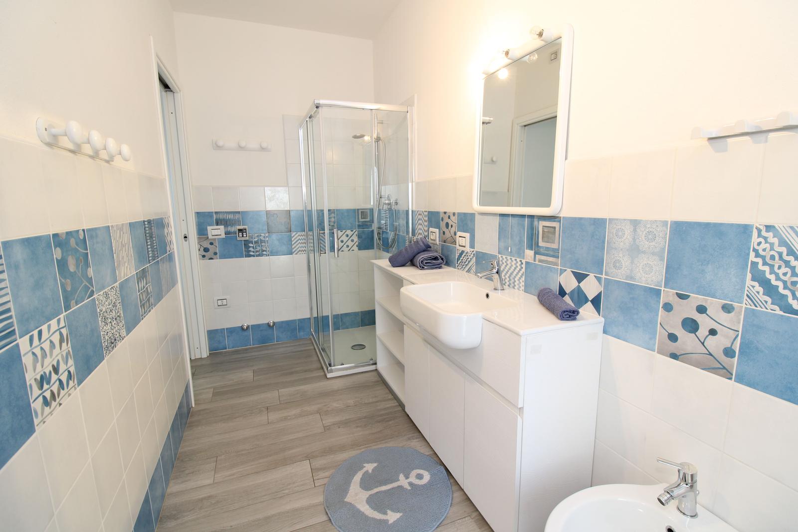 Badezimmer mit Dusche, Waschbecken und Toilette. Wandfliesen in Blau-Weiß-Muster.