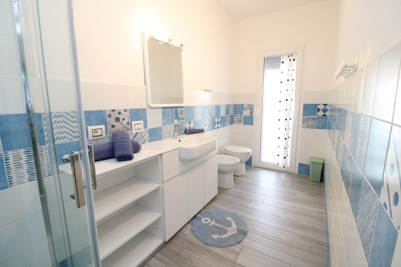 Badezimmer mit Dusche, Waschbecken und Toilette. Blaue Fliesen und grauer Boden.