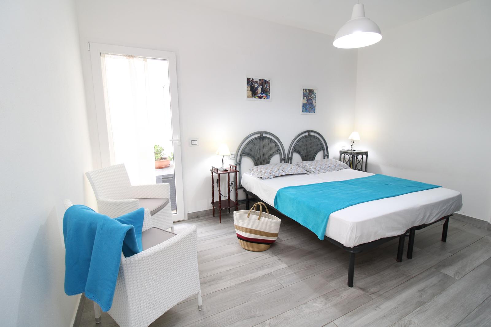 Schlafzimmer mit Doppelbett, zwei Stühlen und Tür zum Balkon.