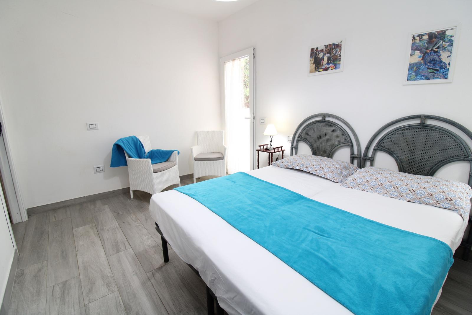 Schlafzimmer mit Doppelbett, zwei Stühlen und Tür zum Balkon.