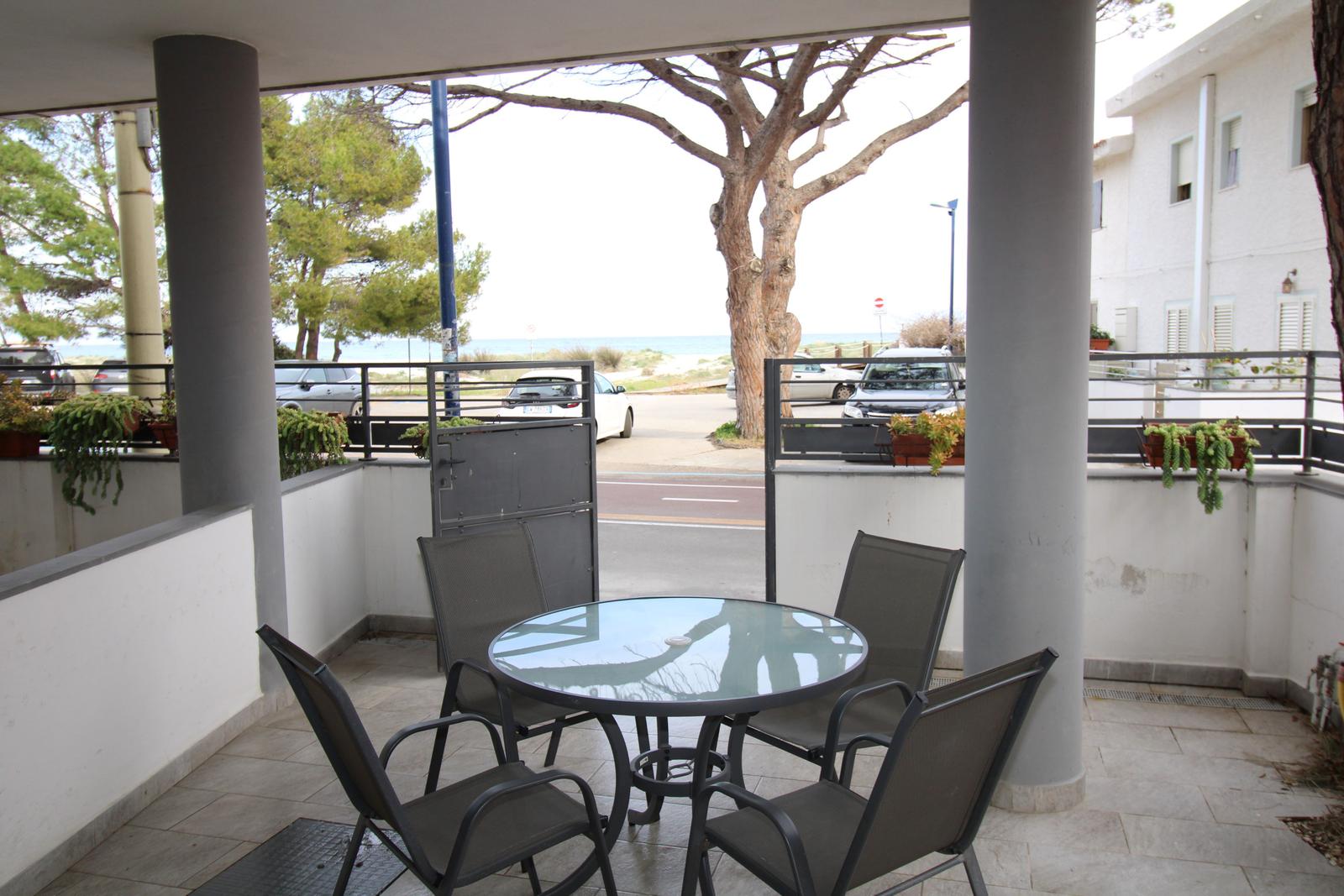 Terrasse mit Tisch und Stühlen, Blick auf Straße und Meer.
