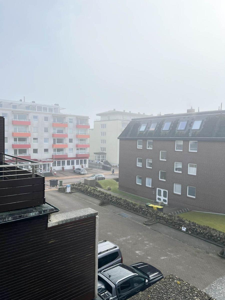Blick auf mehrstöckige Gebäude und geparkte Autos bei nebligem Wetter.