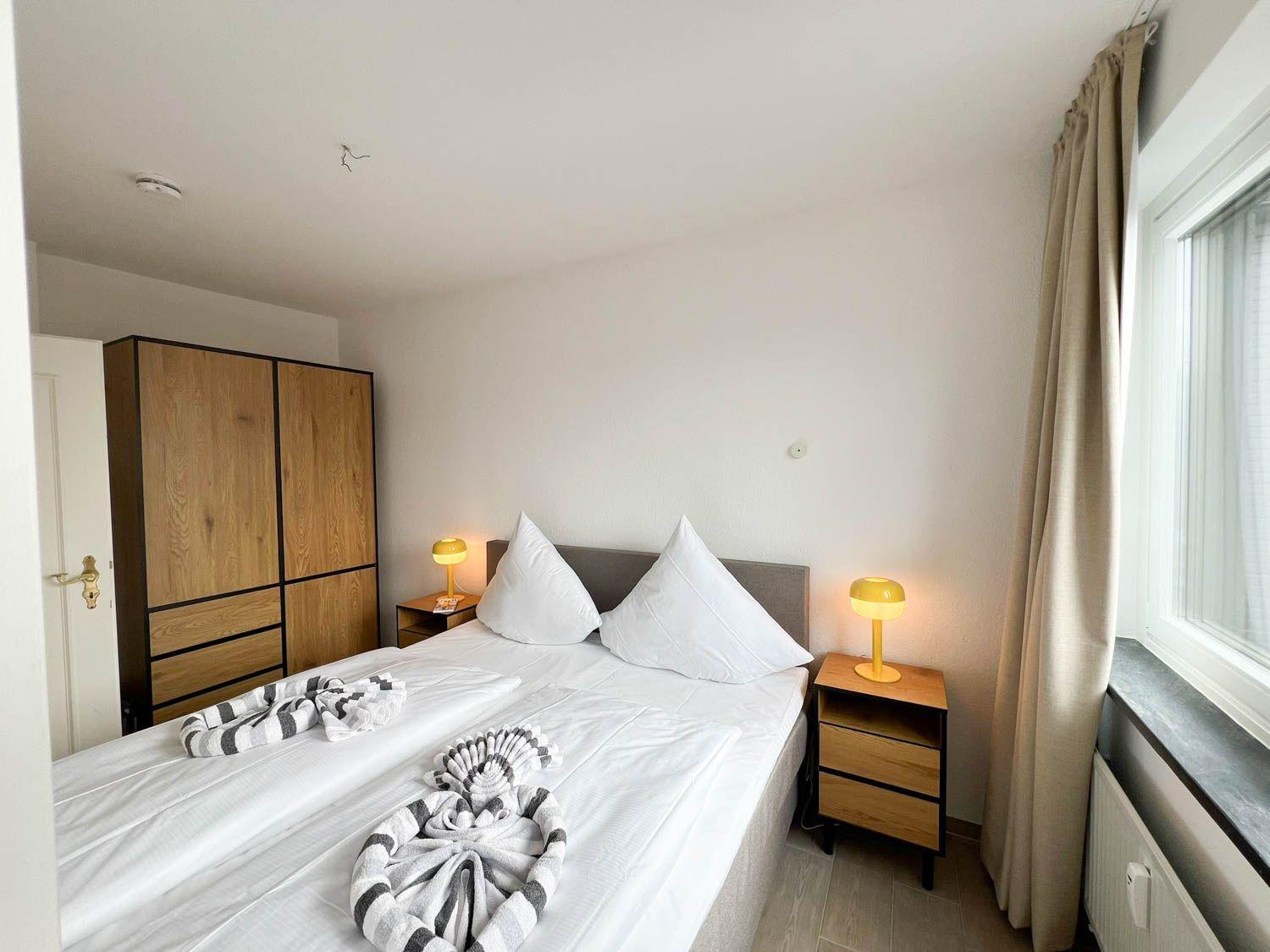 Schlafzimmer mit Doppelbett, zwei Nachttischen und Schrank. Fenster mit Vorhang.