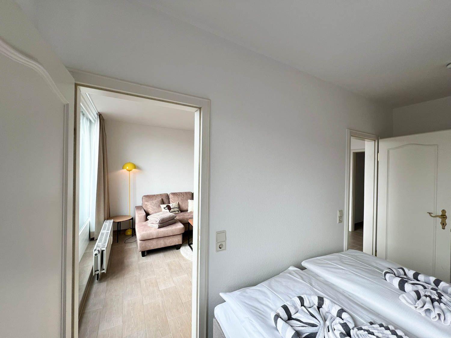 Zimmer mit Bett und Blick in Wohnbereich mit Sofa und Stehlampe.