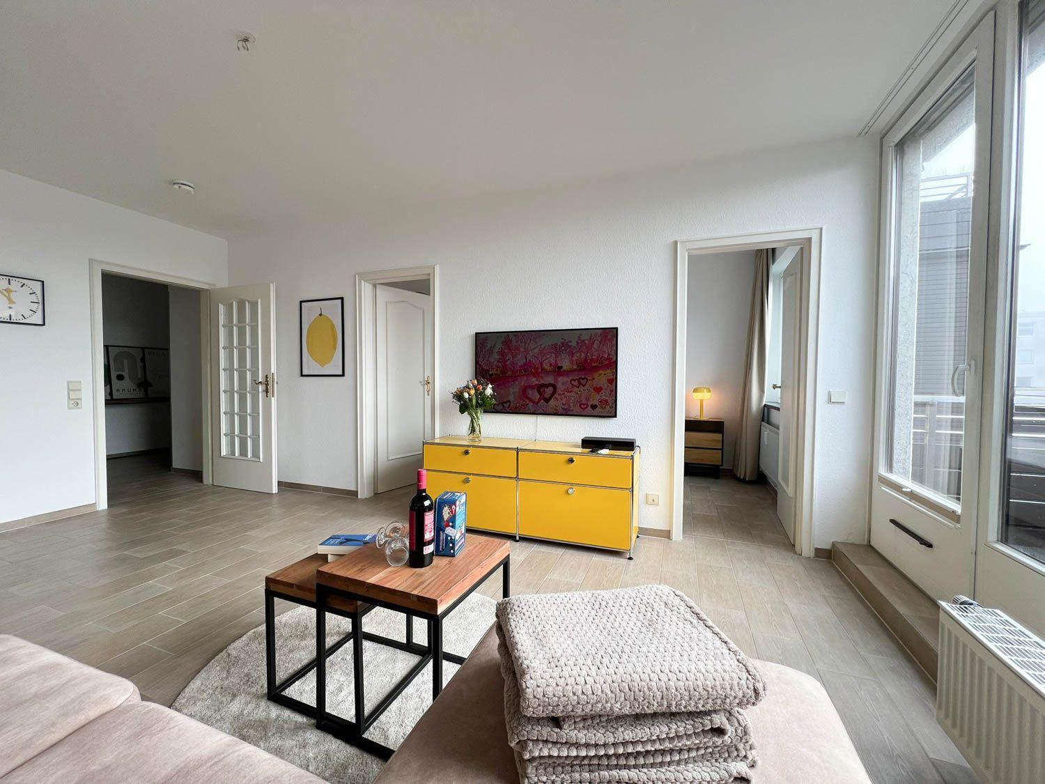 Wohnzimmer mit gelbem Schrank, Fernseher und Glasfront zur Terrasse.