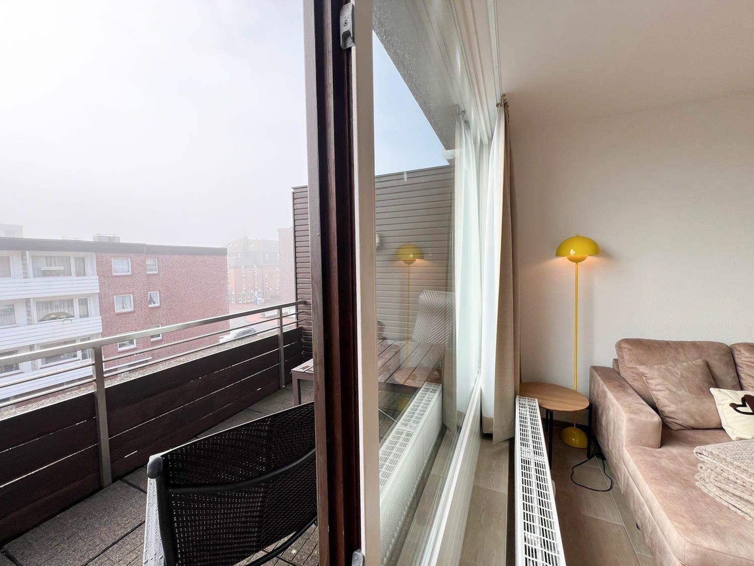 Ein Wohnbereich mit Sofa und gelber Stehlampe neben einer Balkontür.