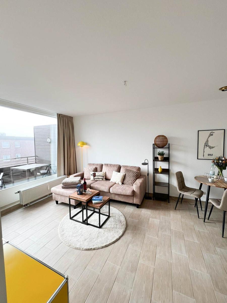 Wohn- und Essbereich mit Sofa, Tisch und Balkonansicht.