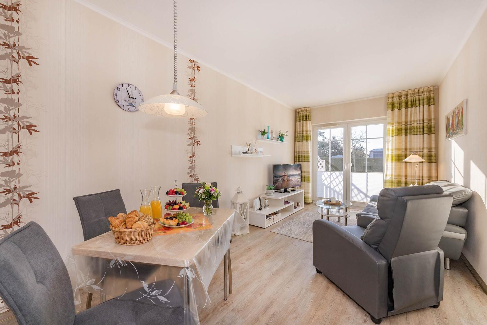 Esszimmer mit Tisch, Stühlen und Frühstück. Wohnzimmer mit Sofa, Fernseher und Balkontür.