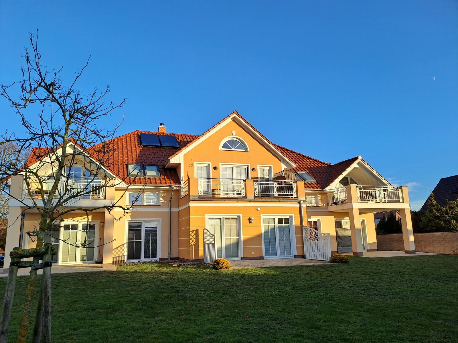 Haus mit Terrasse, Balkon und Garten unter blauem Himmel