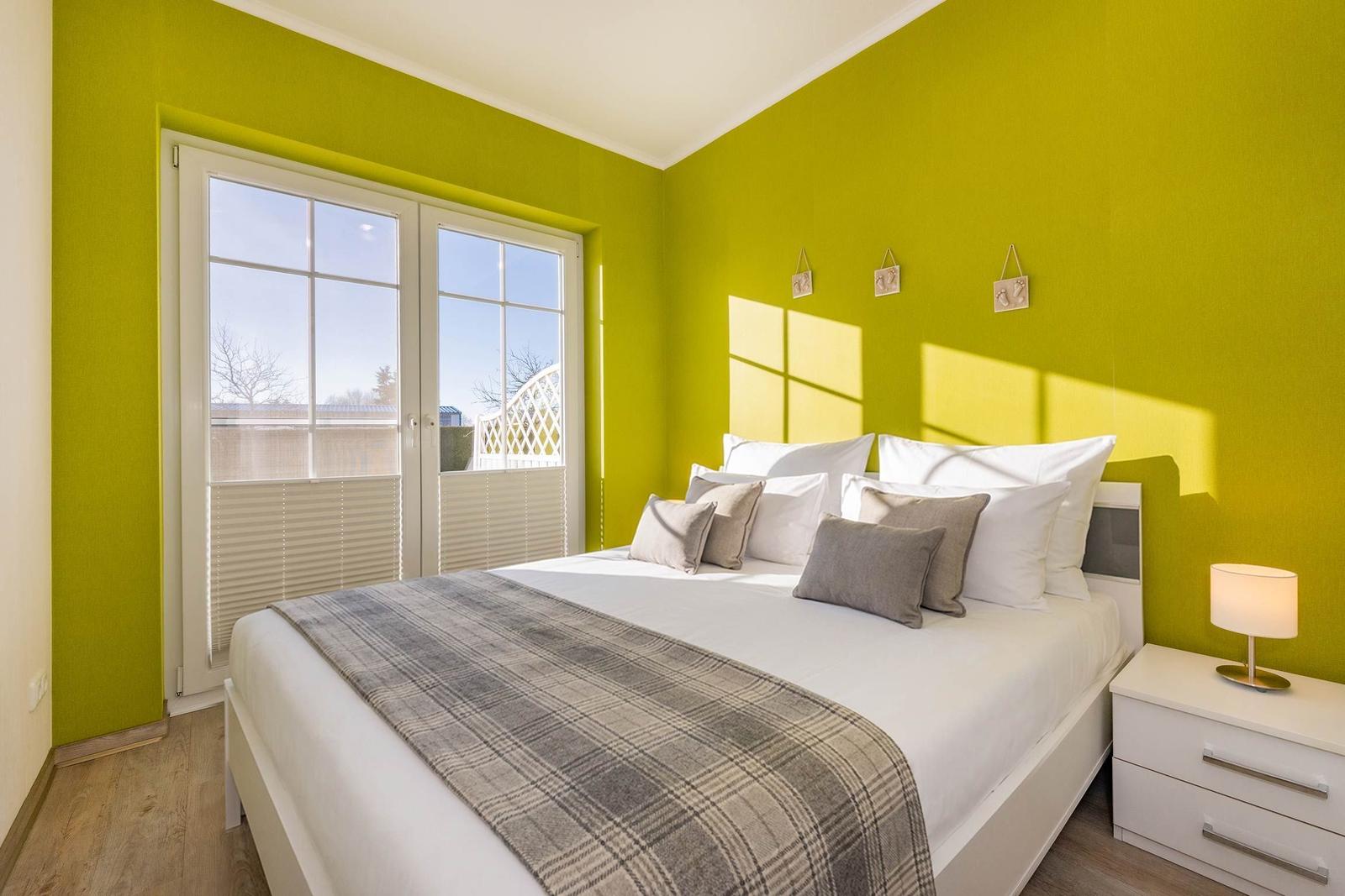 Schlafzimmer mit grüner Wand, Bett und Fenster zur Terrasse.