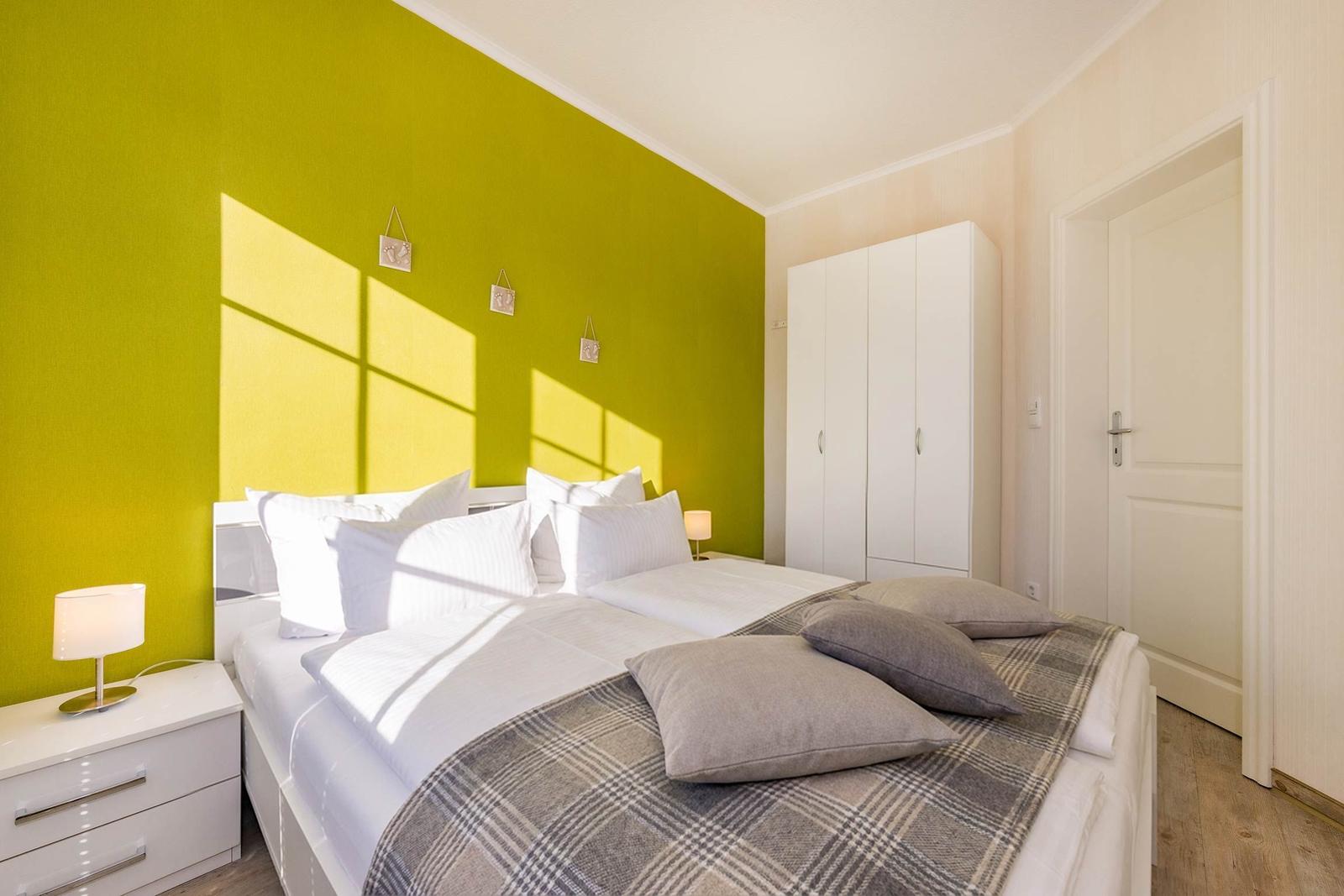 Schlafzimmer mit grünem Wandpaneel, weißem Bett und Kleiderschrank.