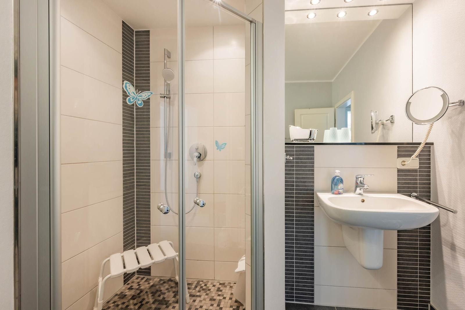 Dusche mit Sitzbank, Waschbecken und Spiegel