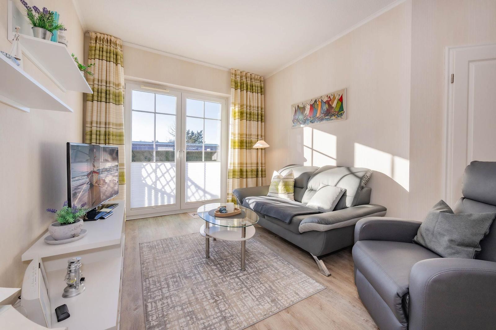 Wohnzimmer mit Sofa, Sessel und TV. Fenster mit Blick auf Balkon.