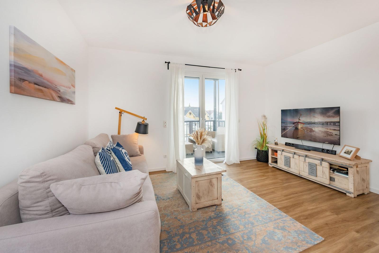 Wohnzimmer mit Sofa, Fernseher und Balkonansicht.