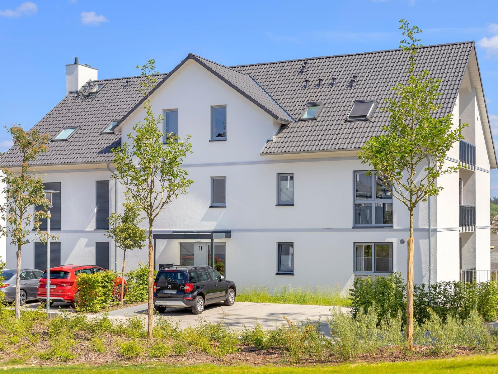 Modernes weißes Mehrfamilienhaus mit Dachfenstern und Parkplatz.
