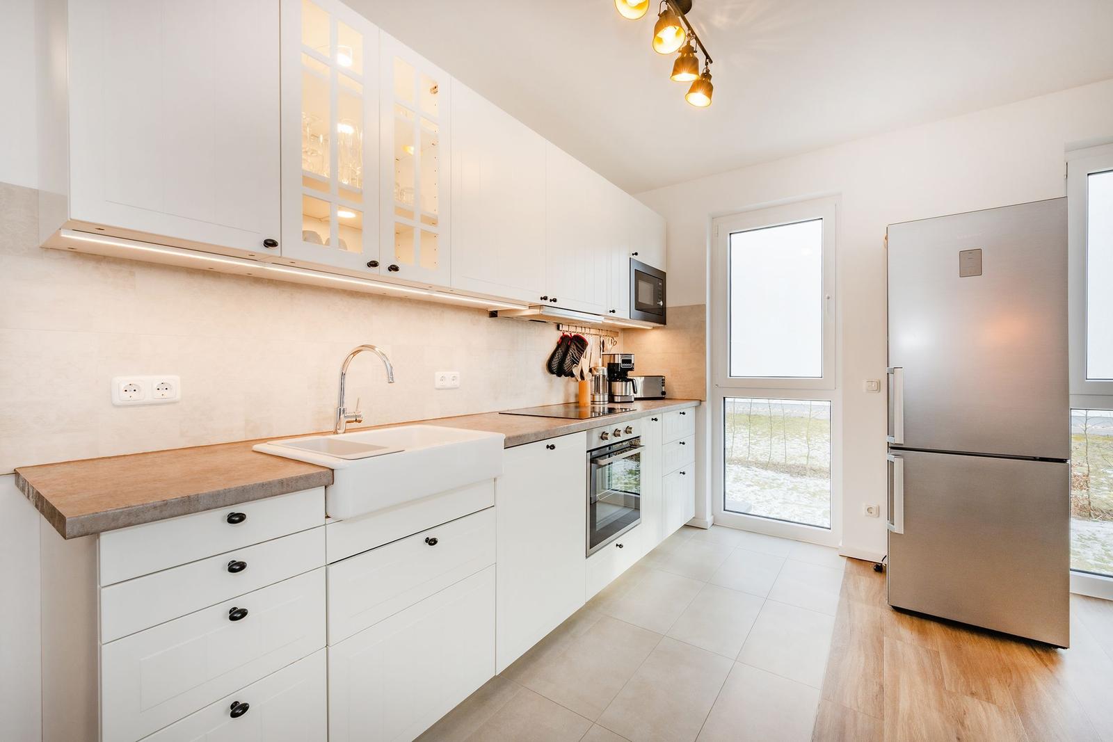 Küche mit weißen Schränken, Edelstahl-Kühlschrank und Fenster zur Außenseite.