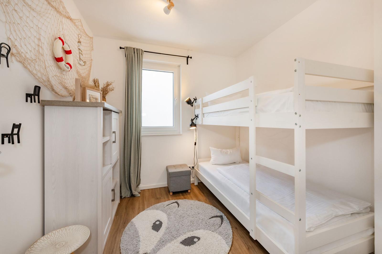 Ein Schlafzimmer mit Doppelstockbett, Fenster, Gardine und dekorativen Wandelementen.
