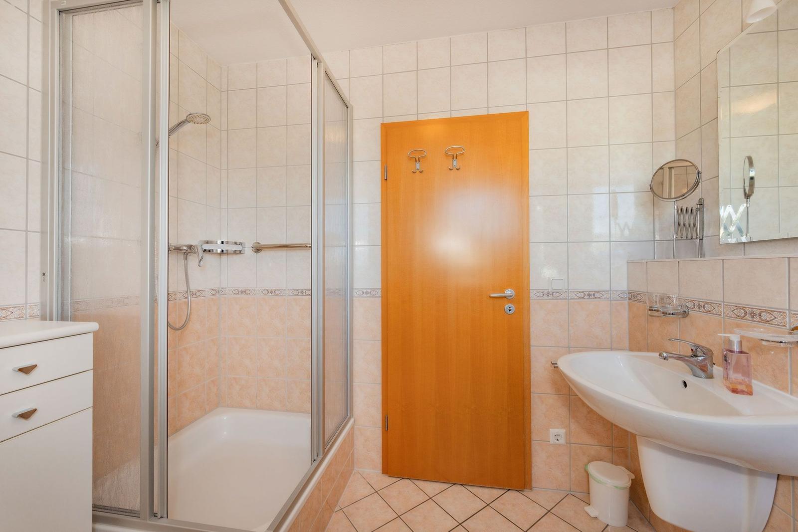 Badezimmer mit Dusche, Waschbecken und Holztür.
