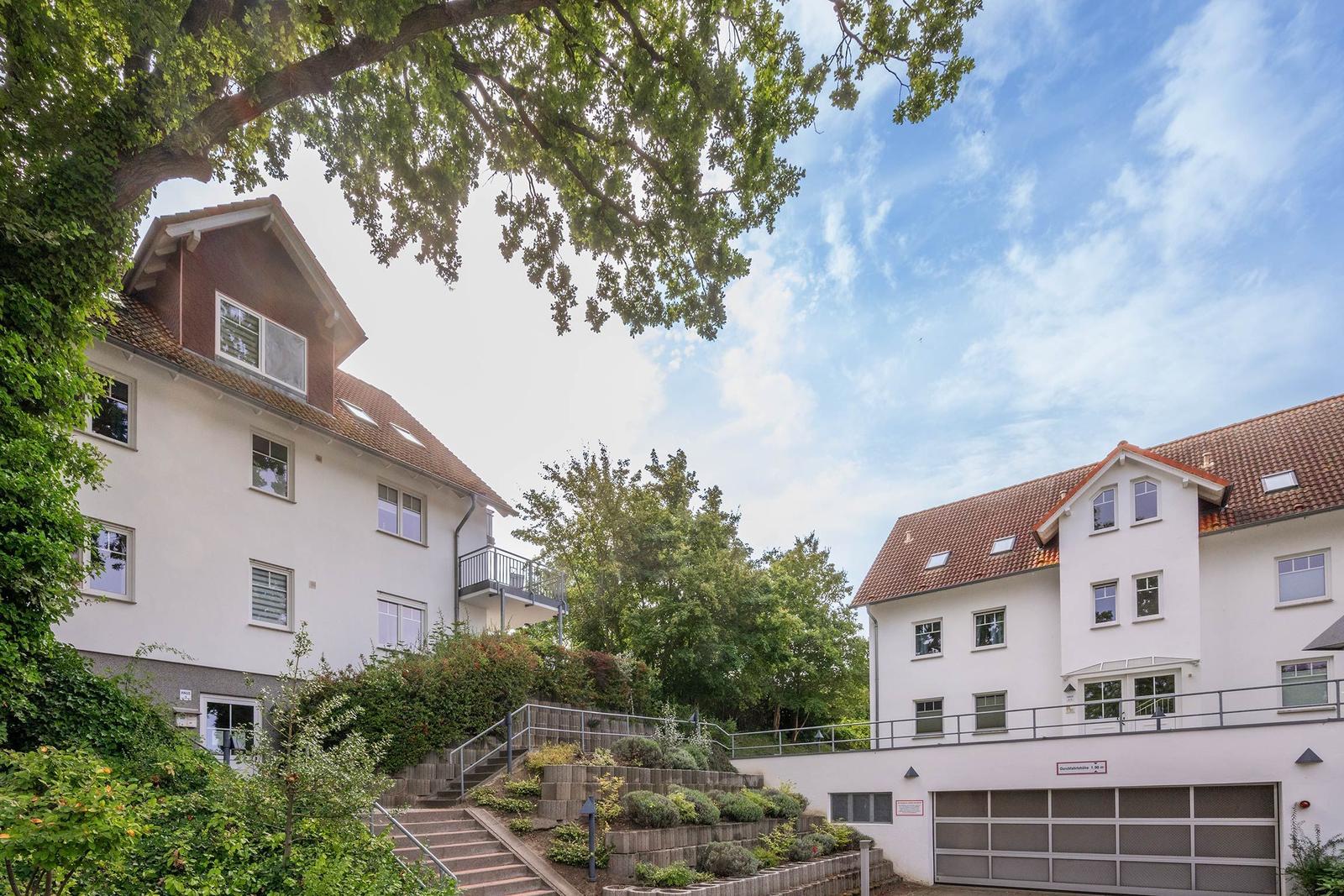 Zwei weiße Gebäude mit roten Dächern und grüner Umgebung unter blauem Himmel.