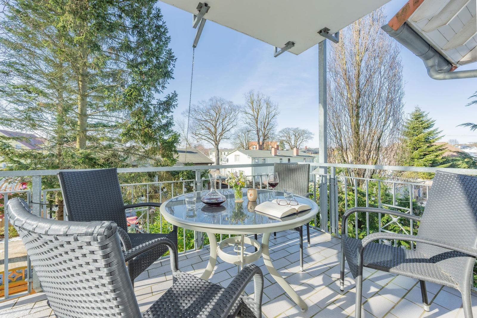 Terrasse mit Tisch und Stühlen, Blick auf Bäume und Häuser.