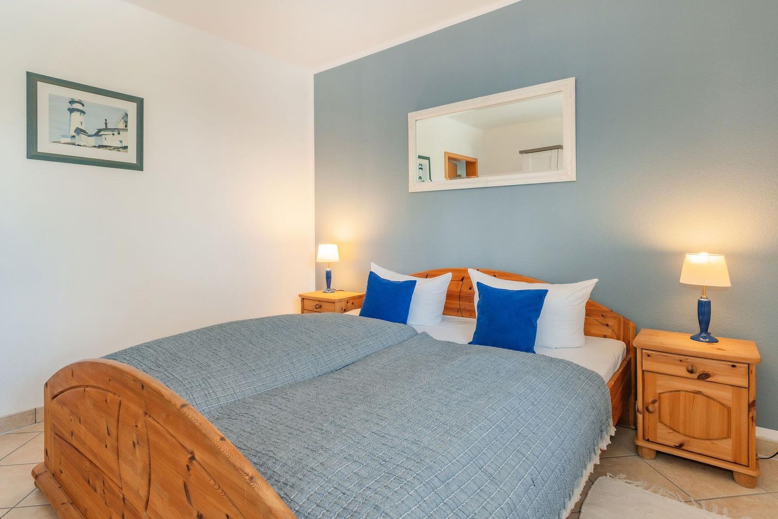 Schlafzimmer mit Holzbett, zwei Nachttischen und Spiegel an der Wand.