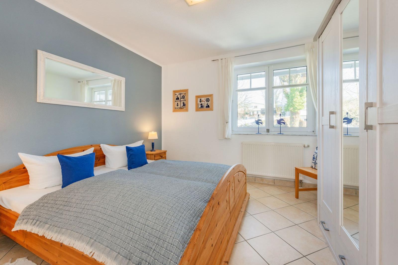 Schlafzimmer mit Holzbett, Fenster und Kleiderschrank.