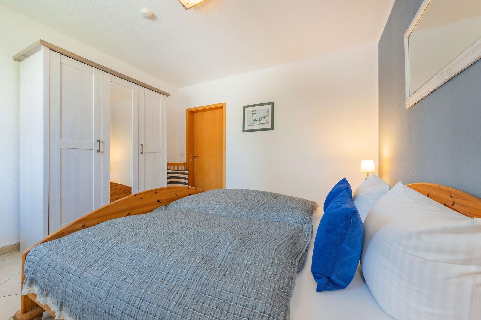 Schlafzimmer mit Bett, Kleiderschrank und Wandspiegel.
