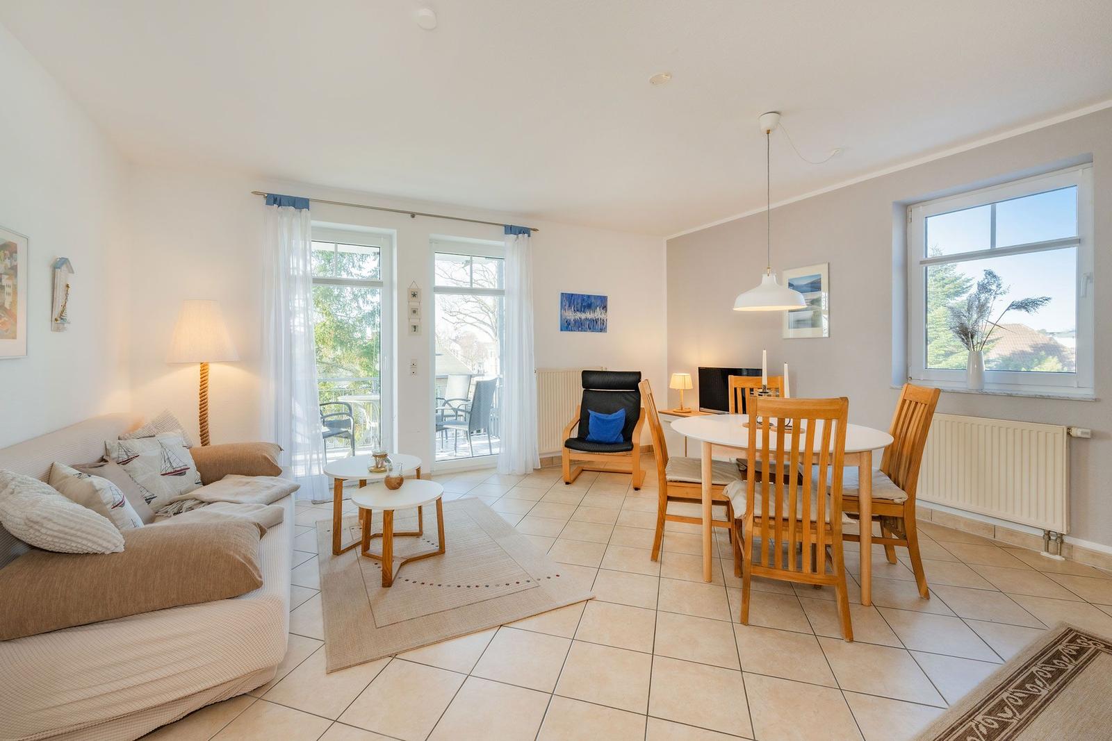 Wohn- und Essbereich mit Sofa, Tisch, Stühlen und Fenstern.