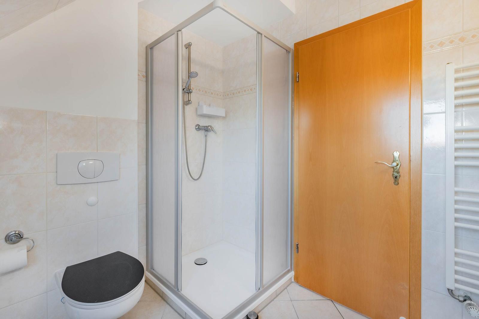 Badezimmer mit Dusche, Toilette und Heizung.