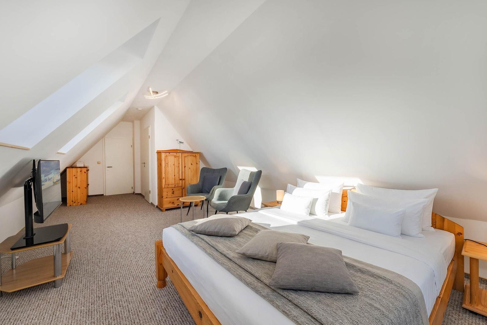 Schlafzimmer mit Dachschrägen, Bett, Fernseher und Sitzgelegenheit.