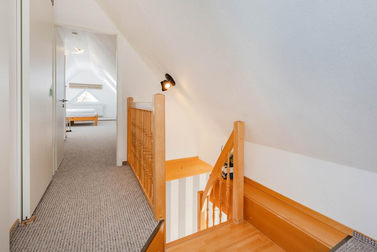 Treppenhaus mit Holzgeländer führt zu einem Schlafzimmer mit Dachfenster.