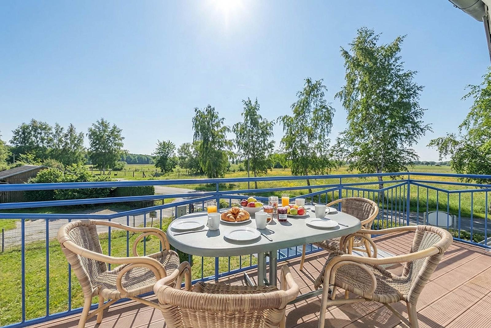 Terrasse mit Tisch und Stühlen, Blick auf grüne Landschaft und Bäume.
