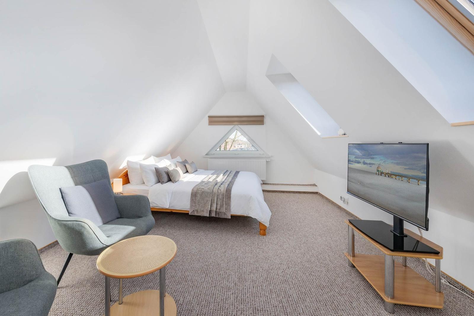 Schlafzimmer mit Dachschrägen, Bett, Sessel und Fernseher.