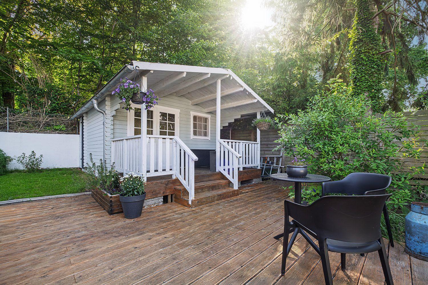 Haus mit Holzterrasse, weißen Geländern und Gartenmöbeln.