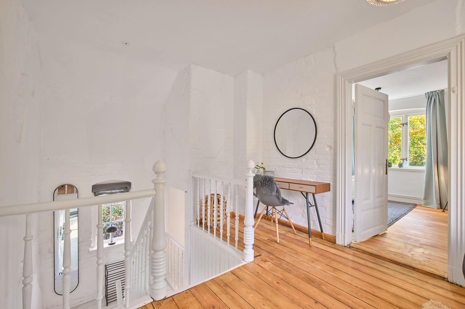 Helle Etage mit Holzboden, weißer Brüstung und Schreibtisch an der Wand.