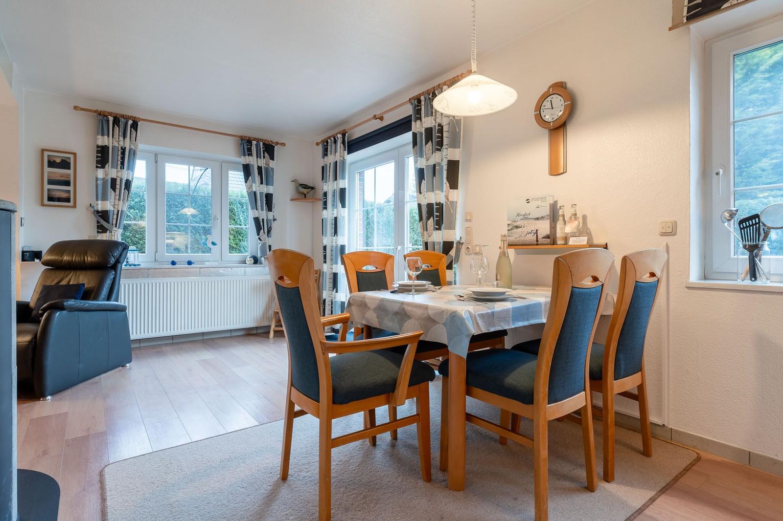 Esszimmer mit Tisch, Stühlen und Fenstern. An der Wand hängt eine Uhr.