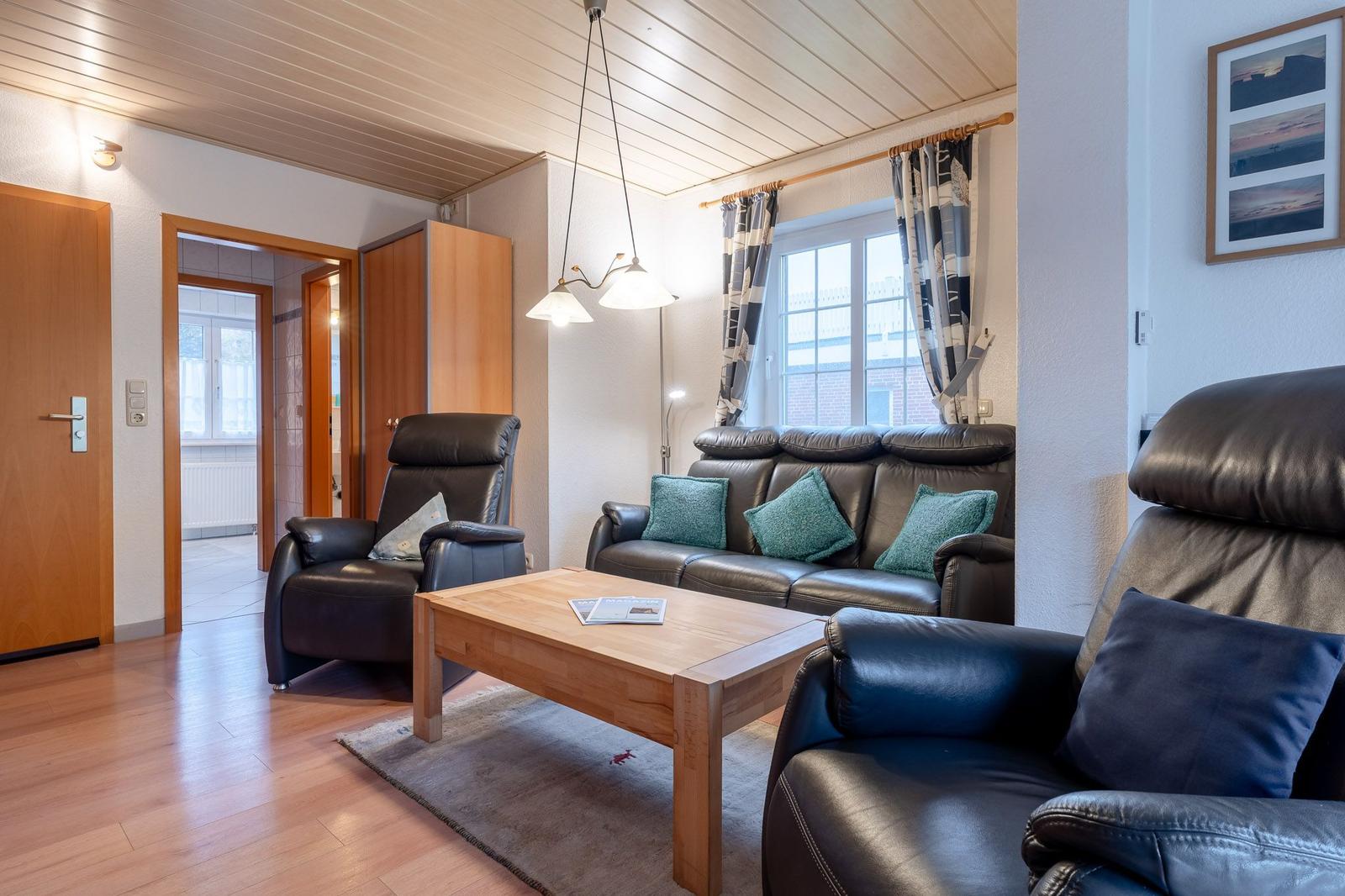 Wohnzimmer mit Ledersofa, zwei Sesseln und Holztisch.