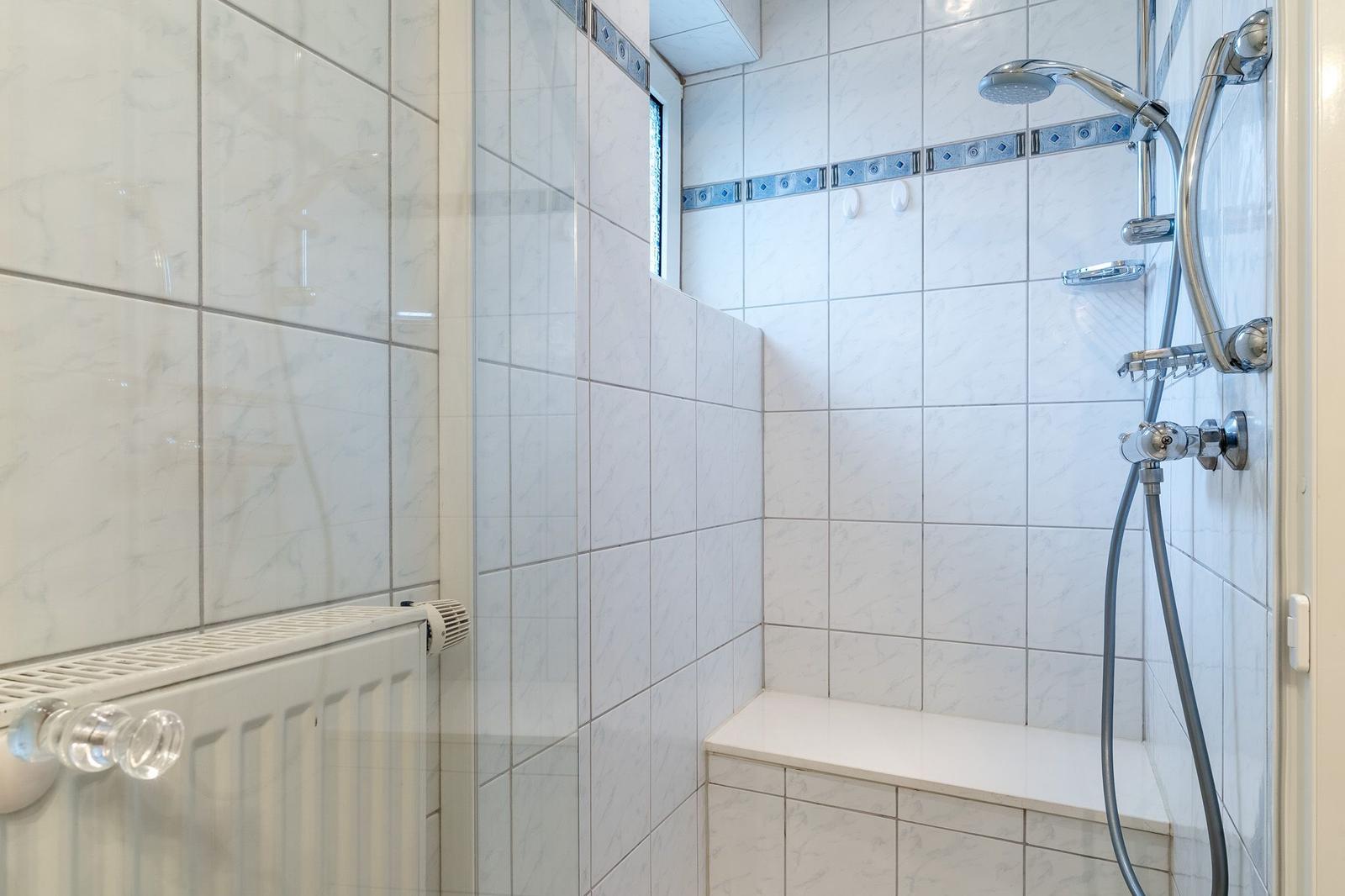 Duschkabine mit Sitzbank, Duschbrause und Heizkörper an der Wand.