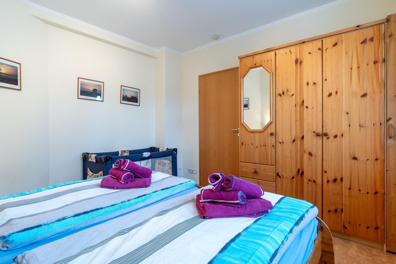 Schlafzimmer mit Bett, Holzschrank und Wandbildern.