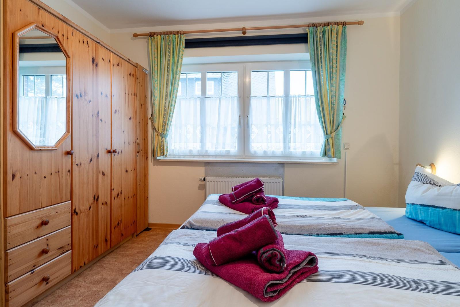 Zimmer mit zwei Betten, Holzschrank und Fenster mit Vorhängen.