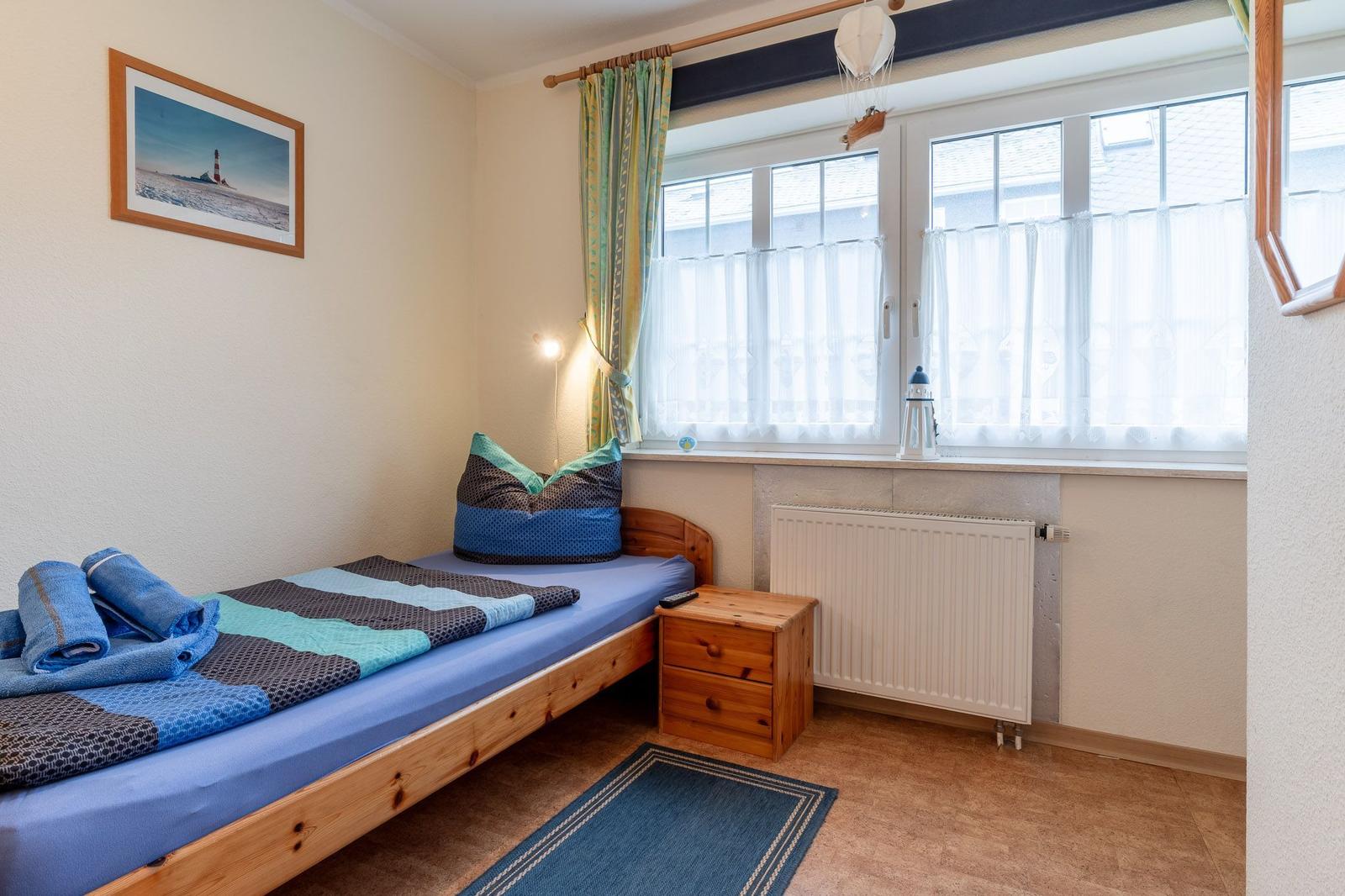 Ein Schlafzimmer mit Bett, Nachttisch und Fenster. Auf dem Bett liegen Handtücher.
