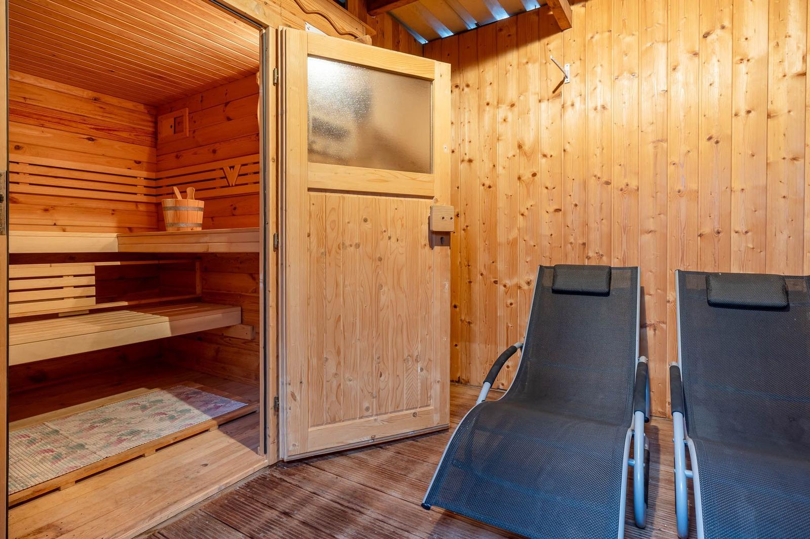 Sauna mit Holzbanken und zwei Liegestühlen vor der Tür.