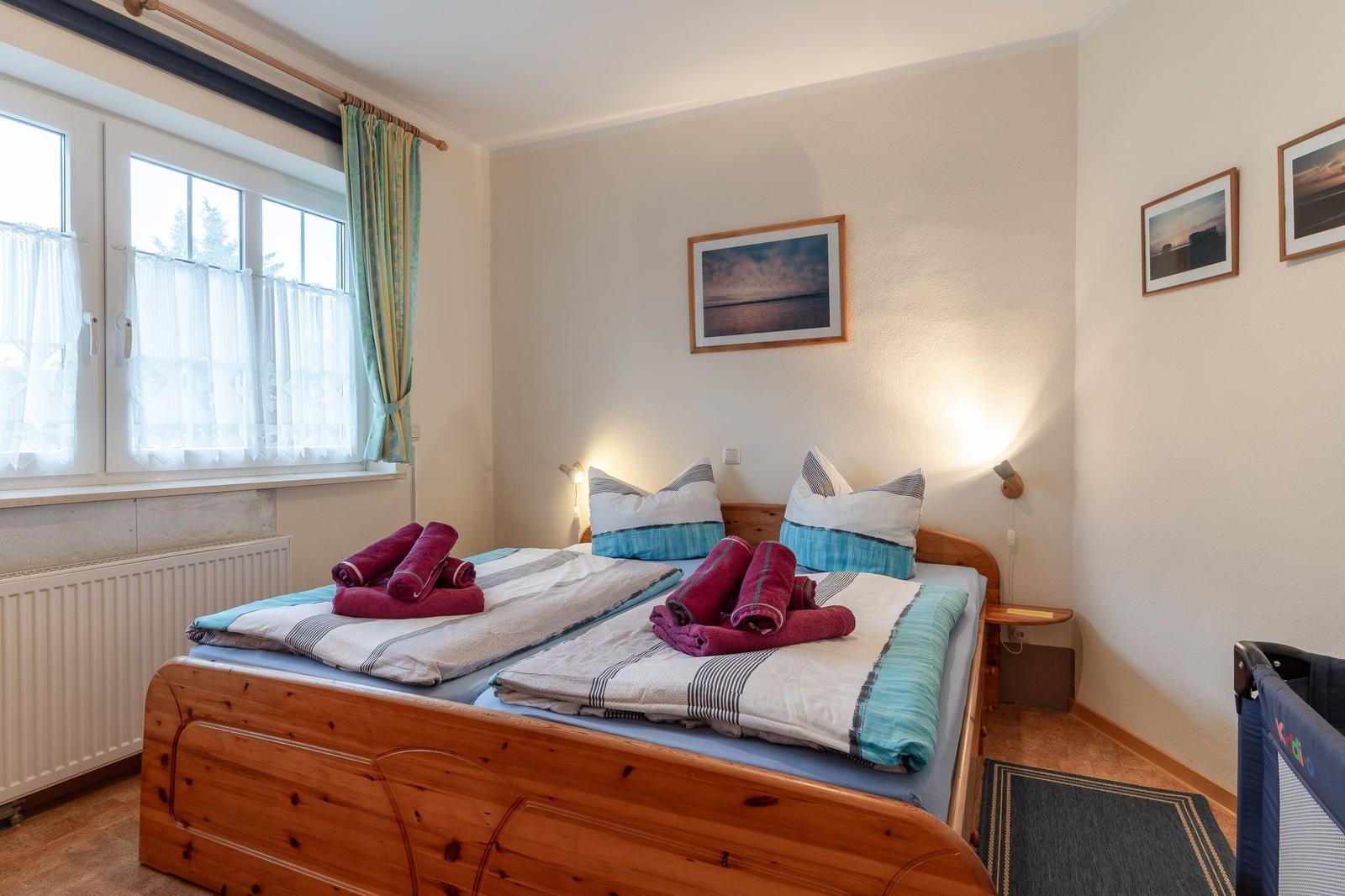 Schlafzimmer mit Holzbett, Fenster und Bildern an der Wand.