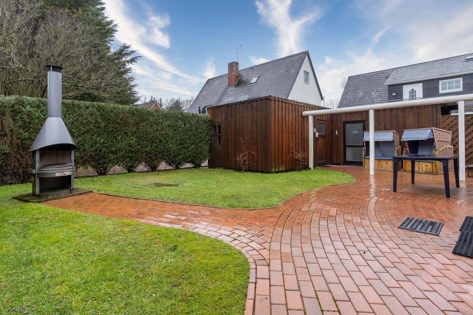 Hinterhof mit Grill, Terrasse und Garten. Holzhaus und Zwerchhaus im Hintergrund.