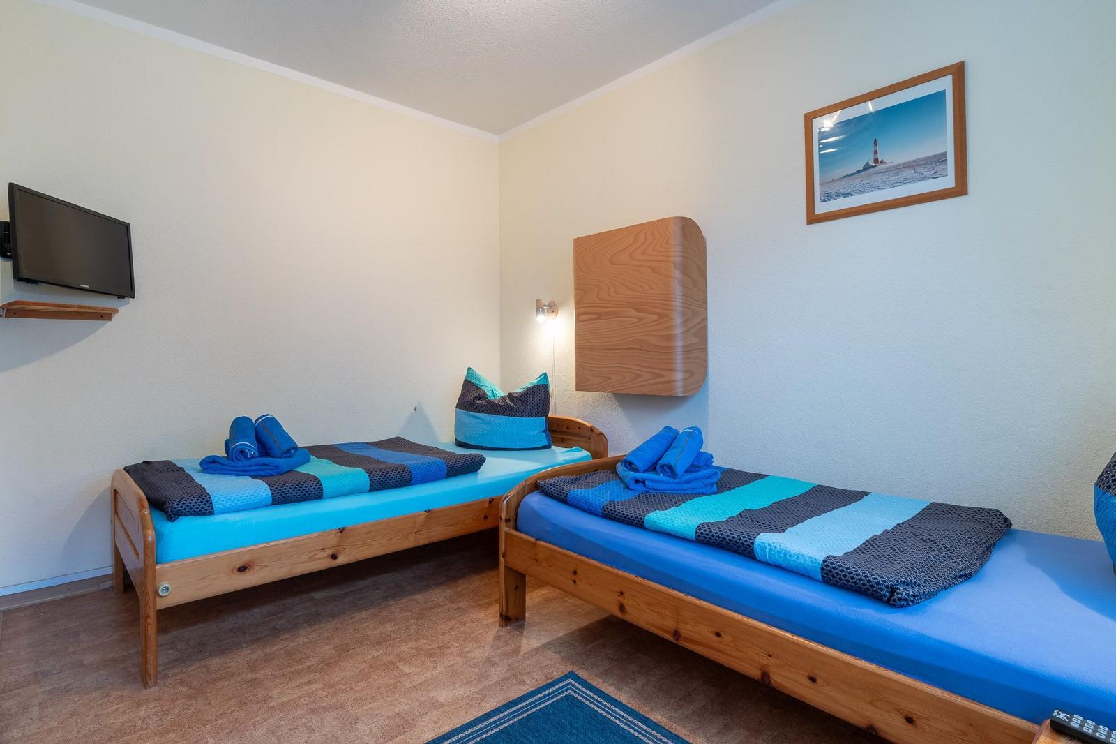 Zwei Betten mit blauen Bettwäschen, Wand-TV und Holzmöbel.