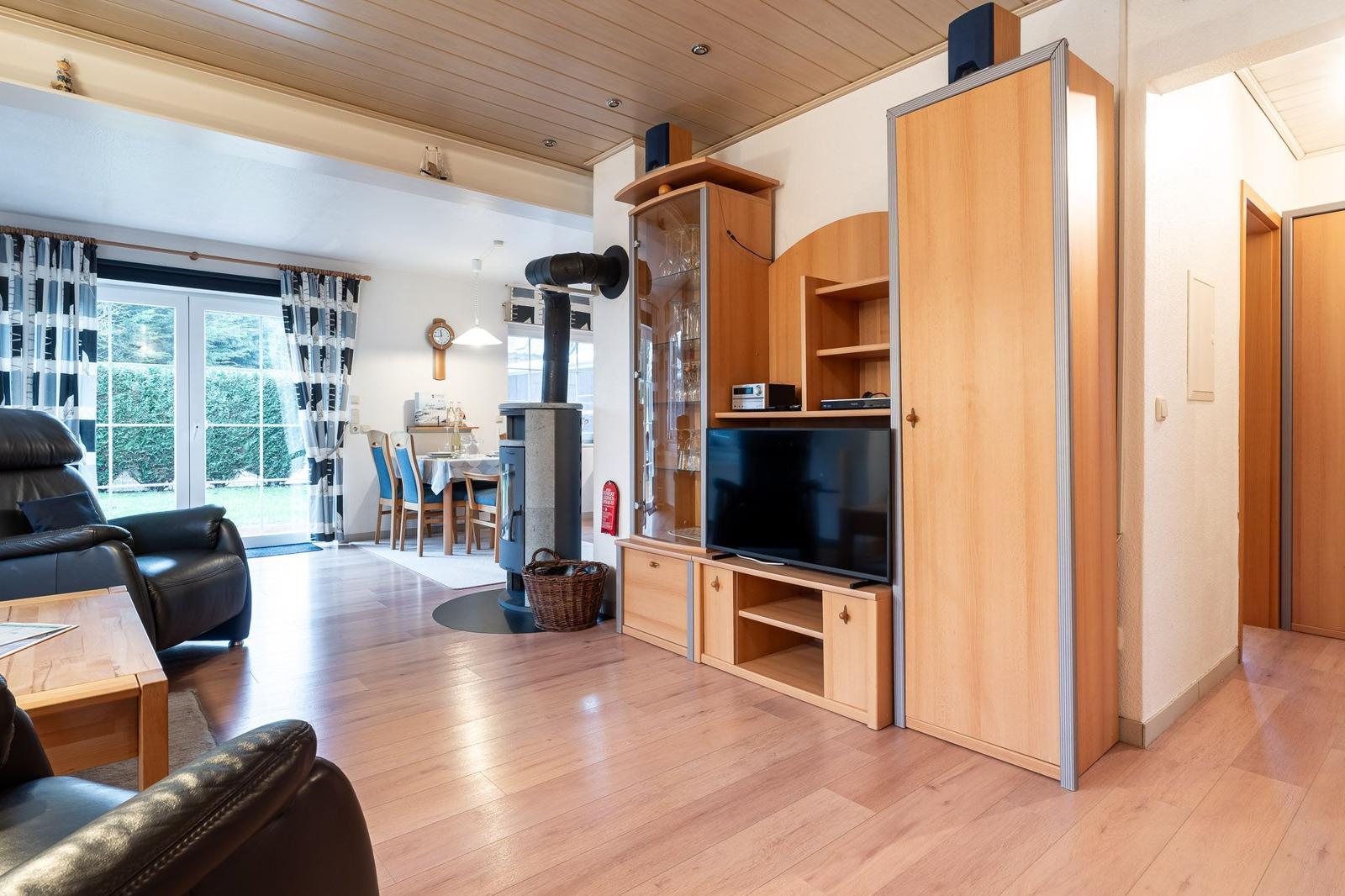 Wohnzimmer mit Holzboden, Sofa, TV und Kaminofen. Essbereich mit Tisch und Stühlen.