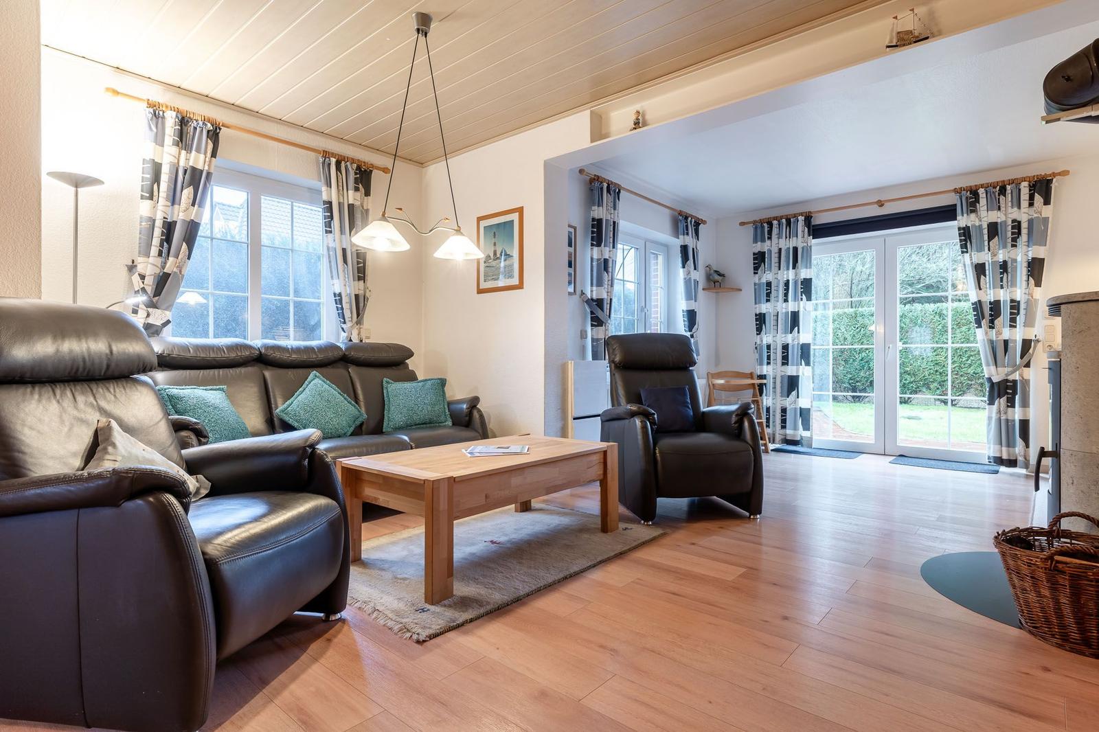 Wohnzimmer mit Ledersofa, Holztisch und Fenstern mit Gardinen.