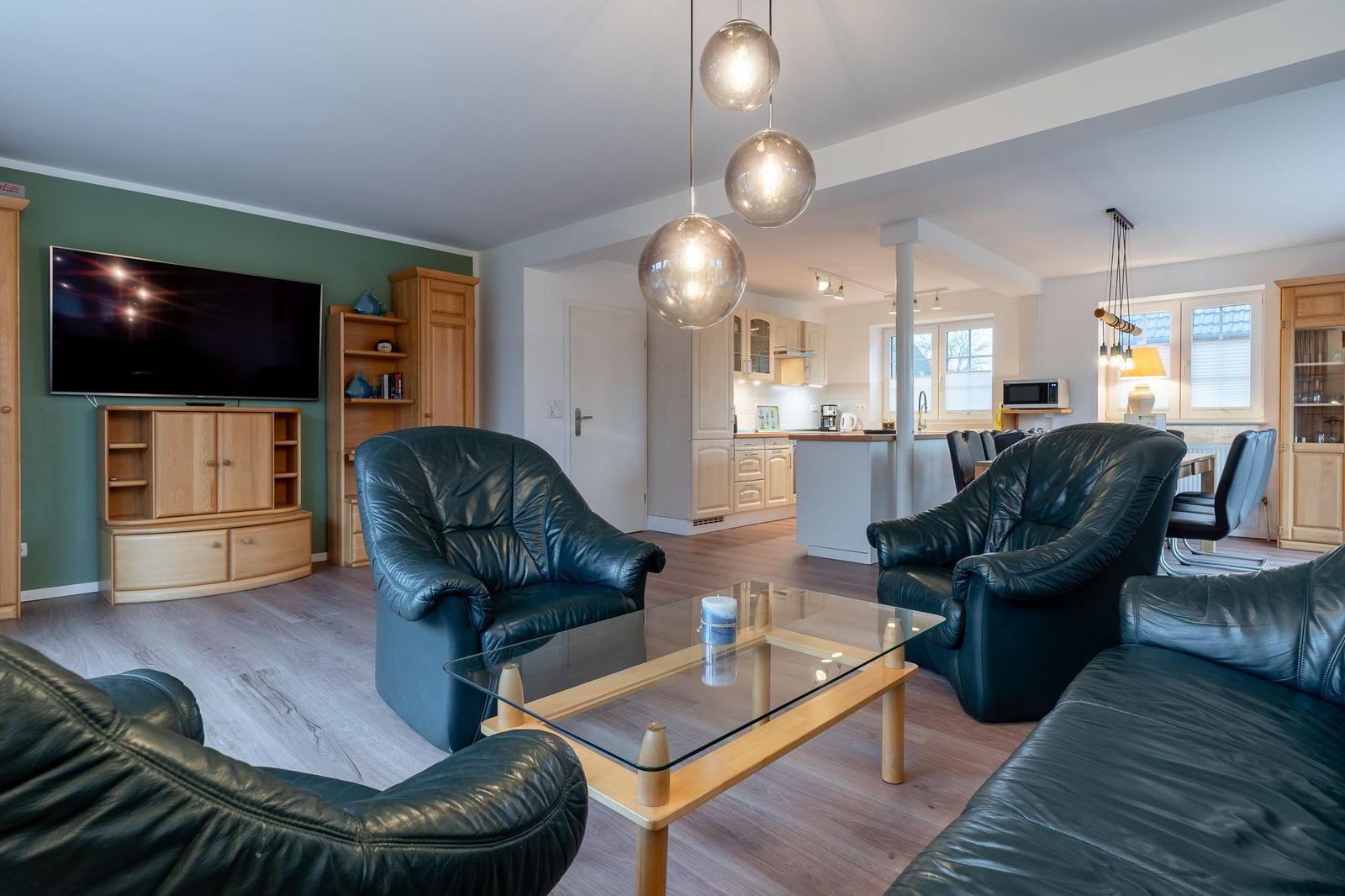 Wohnzimmer mit Ledersofa, Glas-Tisch und Fernseher. Küche im Hintergrund.
